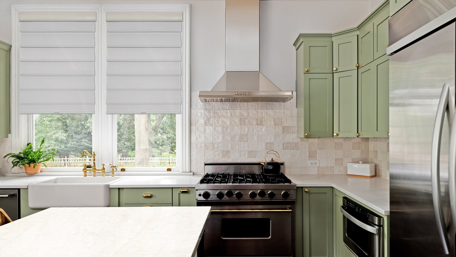 Roller shades in a kitchen with sage green cabinets