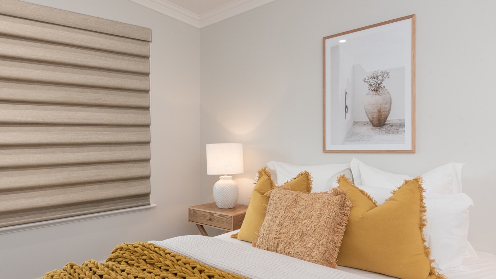 Tan roman shade in a bedroom with mustard pillows