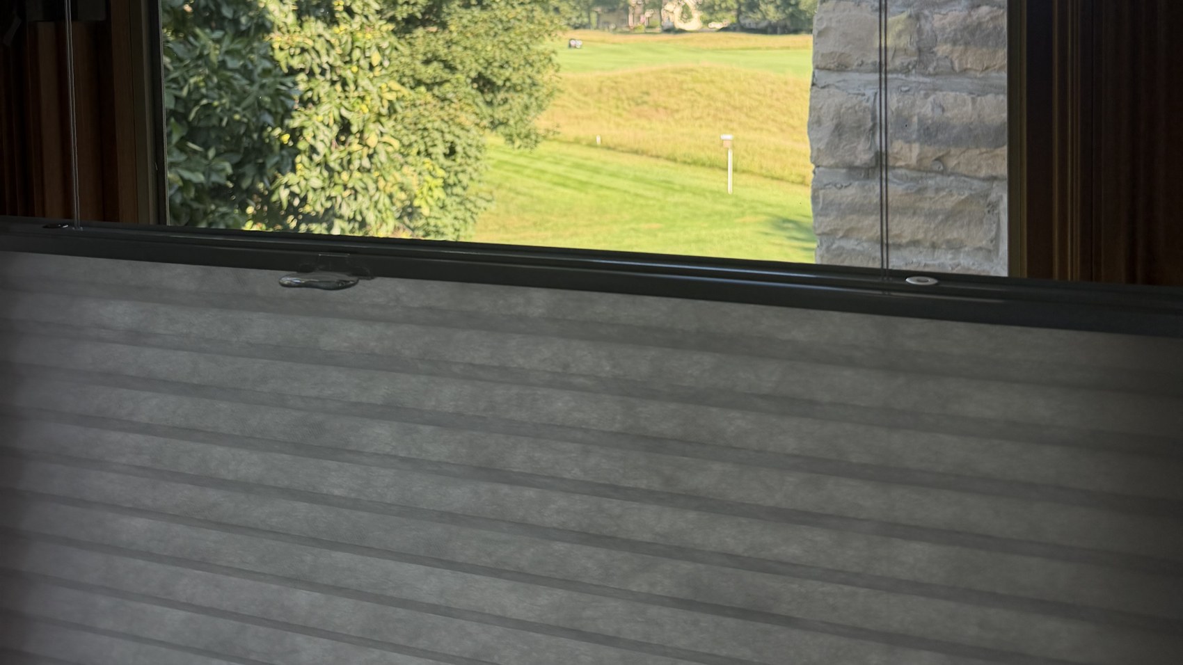 Honeycomb cellular shade raised over a window with a golf course view